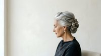 Senior woman with gray hair in elegant updo, wearing dark top, isolated on white background for design use.