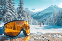 Ski goggles with orange lens reflecting winter landscape, snowy mountains and pine trees with distant skier on slope.