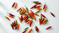 Colorful hot chili peppers scattered on white background. Fresh spicy vegetables for cooking, seasoning and culinary preparations. Isolated organic produce.