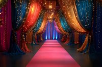 Glamorous red carpet walkway through colorful draped curtains with twinkling fairy lights creating magical entrance for awards ceremony or special event celebration.