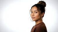 Young mixed-race woman with curly hair in messy bun wearing brown top against white background, natural makeup and confident expression for lifestyle content.