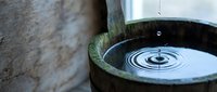 Water droplet creating ripples in wooden bucket with bamboo spout, zen garden meditation concept for spa wellness and mindfulness practices.
