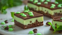 Layered mint chocolate dessert bars with green candy decoration on marble surface. Rich chocolate base topped with mint cream and dark chocolate ganache. Food photography.
