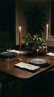Elegant dinner table setting with lit candles, fresh greenery arrangement, and place settings for fine dining or event planning.