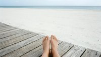 Barefoot woman relaxing on wooden pier overlooking calm sandy beach and ocean, vacation leisure lifestyle concept for travel and summer getaway destinations.