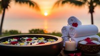 Tropical spa setting with flower bath, towels and candles at sunset beach. Relaxation wellness retreat concept for luxury resort treatments and meditation.