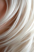 Flowing platinum blonde hair strands in macro shot creating abstract wavy pattern with soft brown background, suitable for beauty and haircare advertising.