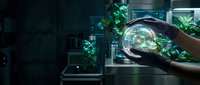 Hand holding glowing globe with digital network connections and green plants in modern tech workspace, representing sustainable technology, innovation, and environmental consciousness.