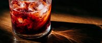 Dark red cocktail with ice in a rocks glass on a wooden bar surface, dramatic moody lighting highlighting the rich color of the drink.