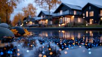 Modern lakeside houses with glowing windows reflected in water at dusk, orange autumn trees and bokeh light effects create serene evening atmosphere.