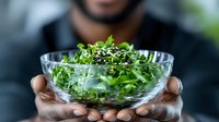 Fresh microgreens and sprouts in crystal bowl held by chef hands, healthy organic salad ingredients against dark background, selective focus on greens.