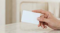 Hand holding blank white card on wooden table surface for business card mockup and branding presentation.