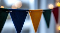 Colorful triangle bunting flags in green, navy blue and yellow against blurred bokeh background create festive party atmosphere. Decorative garland for celebration events.