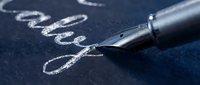 Fountain pen with silver nib writing cursive script on dark blue paper, suitable for stationery, writing, education, and business communication designs.