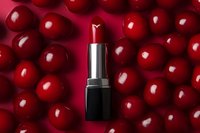 Red lipstick on vibrant cherry background with scattered fresh berries creating luxurious cosmetic flatlay composition for beauty and makeup advertising.