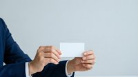 Businessman in dark suit holding blank white business card, isolated on gray background for corporate branding and professional design use.