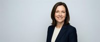 Professional businesswoman in navy blazer smiling confidently against clean white background, corporate headshot for marketing materials.