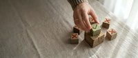 Wooden alphabet blocks with letters scattered on textured surface as hand reaches to arrange educational toys for early childhood learning development.