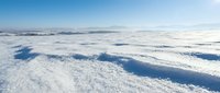 Aerial view of snow-covered landscape with blue shadows and distant mountains under clear sky, suitable for winter backgrounds and environmental projects.