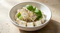 Fresh tofu cubes with herbs and black pepper seasoning in ceramic bowl ready for healthy cooking and meal preparation.