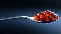 Fresh red caviar on silver spoon against dark background, luxury seafood close up with reflective surface and dramatic lighting for gourmet food presentation.