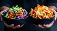 Hands holding black bowls with fresh poke bowl and crispy nachos with cheese sauce. Healthy and indulgent food choices showing contrast in modern cuisine.