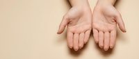 Open female hands cupped together in receiving gesture on neutral beige background, symbolizing care, support, giving and protection concepts.