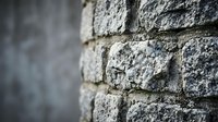 Close-up of weathered gray stone brick wall with rough textured surface and mortar joints showing architectural detail and construction materials.