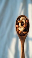 Wooden spoon filled with mixed nuts and dried fruits including cashews, almonds, hazelnuts and raisins on soft blue background with natural shadows.