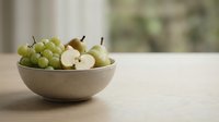 Green grapes and sliced apples in a beige ceramic bowl on wooden table, fresh fruit arrangement for food and healthy eating concepts.