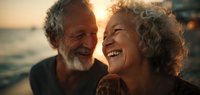 Happy senior couple laughing together at sunset by ocean. Elderly man and woman enjoying romantic moment on beach during golden hour vacation.