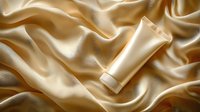 Luxurious cream tube on flowing golden silk fabric background with soft waves and folds creates elegant cosmetic product presentation for beauty industry.