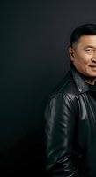 Middle-aged Asian man wearing black leather jacket against dark background, smiling confidently. Portrait suitable for business, lifestyle, and professional applications.