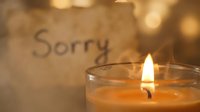 Burning candle with warm golden bokeh and a handwritten sorry note in soft focus, evoking apology, sympathy, and emotional healing.