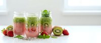 Layered green and pink smoothies in glass jars with fresh strawberries, kiwi and mint on white kitchen counter for healthy breakfast concept.