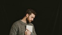 Thoughtful bearded man in cozy sweater holding white mug, enjoying warm beverage in moody lighting for lifestyle and comfort concepts.