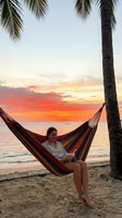Young woman relaxing in colorful striped hammock on tropical beach at sunset with palm trees and ocean waves for vacation and travel concepts.