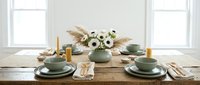 Elegant dining table setting with sage green plates, pampas grass centerpiece and white flowers in bright modern interior for home decor inspiration.