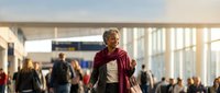 Senior African American woman walking through modern airport terminal with luggage during golden hour travel journey.