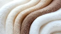Soft folded towels in cream and brown shades creating gentle waves and curves, showing texture and layers of plush cotton terry cloth material.
