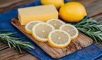 Fresh sliced lemons with butter block and rosemary sprigs on rustic wooden cutting board against blue napkin, food preparation concept.