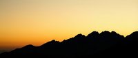 Silhouetted mountain range against warm golden sunset sky, creating dramatic landscape scenery for travel and nature design projects.