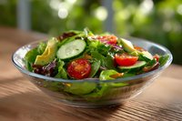 Fresh garden salad with sliced cucumber, cherry tomatoes, mixed greens and avocado in glass bowl on wooden table with natural sunlight background.