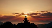 Silhouette of person meditating on mountain peak during golden sunset with dramatic clouds and layered mountain ranges creating peaceful spiritual scene.