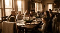 Multi-generational family enjoying Thanksgiving dinner together around wooden dining table in warm, cozy home with natural lighting and traditional decor.