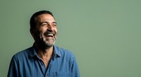 Middle-aged man with dark hair and beard wearing blue casual shirt, smiling against green background for portrait and lifestyle use.