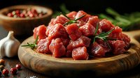 Raw beef cubes with rosemary and garlic on wooden cutting board, fresh meat chunks ready for cooking, dark moody food photography styling.