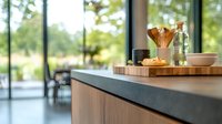 Modern kitchen counter with pour-over coffee setup, fresh pastry, and natural light streaming through large windows, creating warm morning atmosphere in contemporary home.