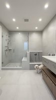 Modern luxury bathroom interior with glass shower, floating vanity, recessed lighting and small white dog on gray tile floor for home design inspiration.