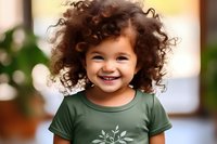 Cheerful mixed race child with curly hair wearing green t-shirt smiling brightly against blurred background. Natural lighting highlights joyful expression.